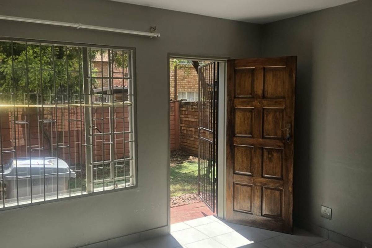 An empty living room featuring tiled flooring, security bars on the windows, and direct access to the rear garden through a wooden door.