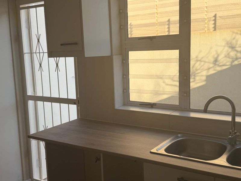 A clean kitchen area featuring a laminate countertop, stainless steel sink with mixer tap, and built-in cabinetry, illuminated by natural light.