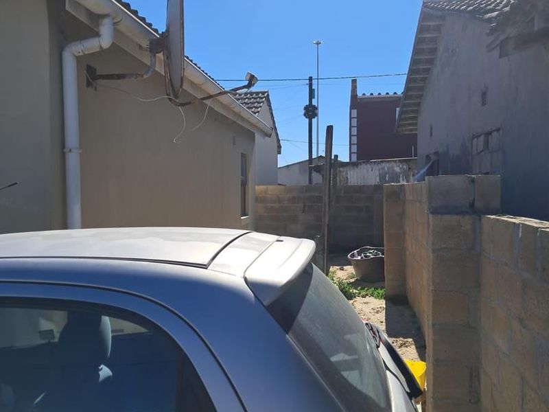 A narrow side or rear exterior passage featuring a cinder block boundary wall, guttering, and a satellite dish mounted on the building exterior.