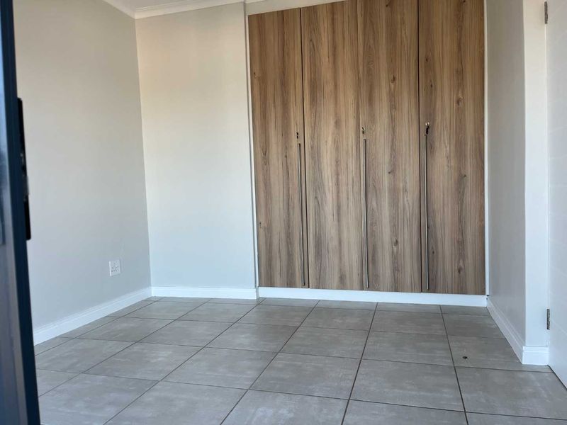 A clean, empty bedroom featuring modern wood-finish built-in cupboards and neutral tiled flooring.