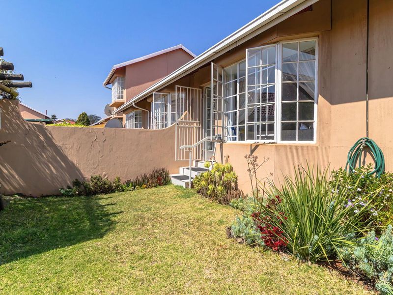 Rear exterior view of the townhouse featuring a small private garden, boundary wall, and access to the living area via a security gate.