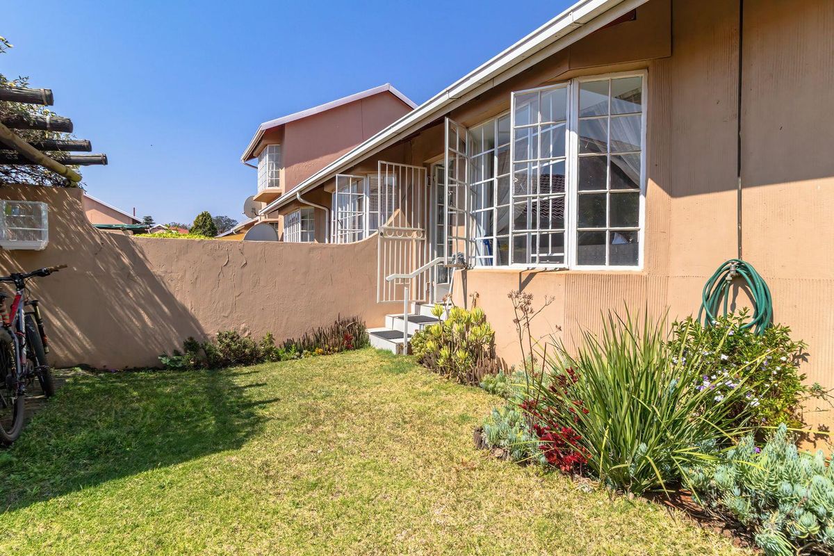 Rear exterior view of the townhouse featuring a small private garden, boundary wall, and access to the living area via a security gate.