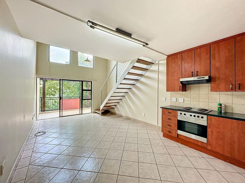 Open-plan living area featuring a kitchen with built-in cabinetry, tiled floors, and a staircase leading to an upper level with balcony access.