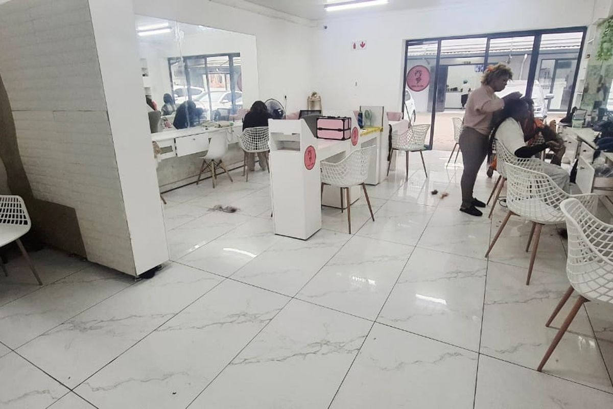 Open-plan commercial salon space featuring tiled flooring, built-in vanity stations with large mirrors, and aluminium framed glass doors providing natural light.