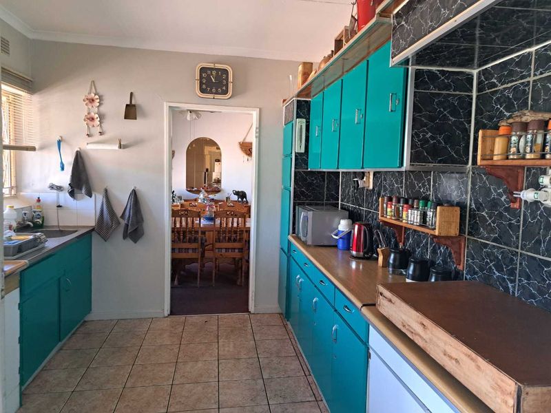 A functional kitchen featuring teal cabinetry, dark marble-effect tiled splashbacks, and tiled flooring, with a direct view into the adjacent dining area.