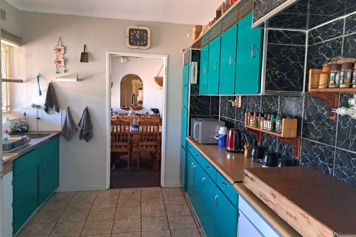 A functional kitchen featuring teal cabinetry, dark marble-effect tiled splashbacks, and tiled flooring, with a direct view into the adjacent dining area.