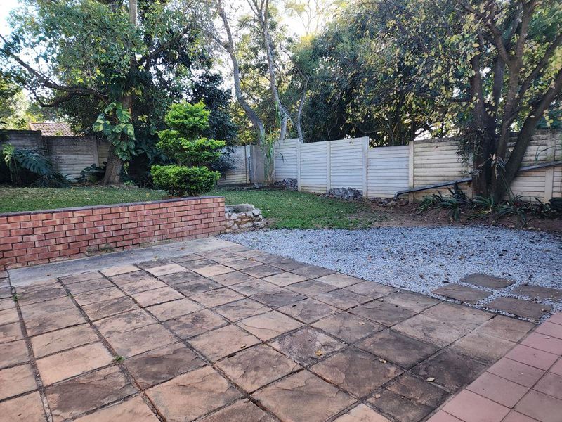 A private rear garden featuring a paved patio area, brick retaining wall, and established trees, offering potential for outdoor entertainment and landscaping.