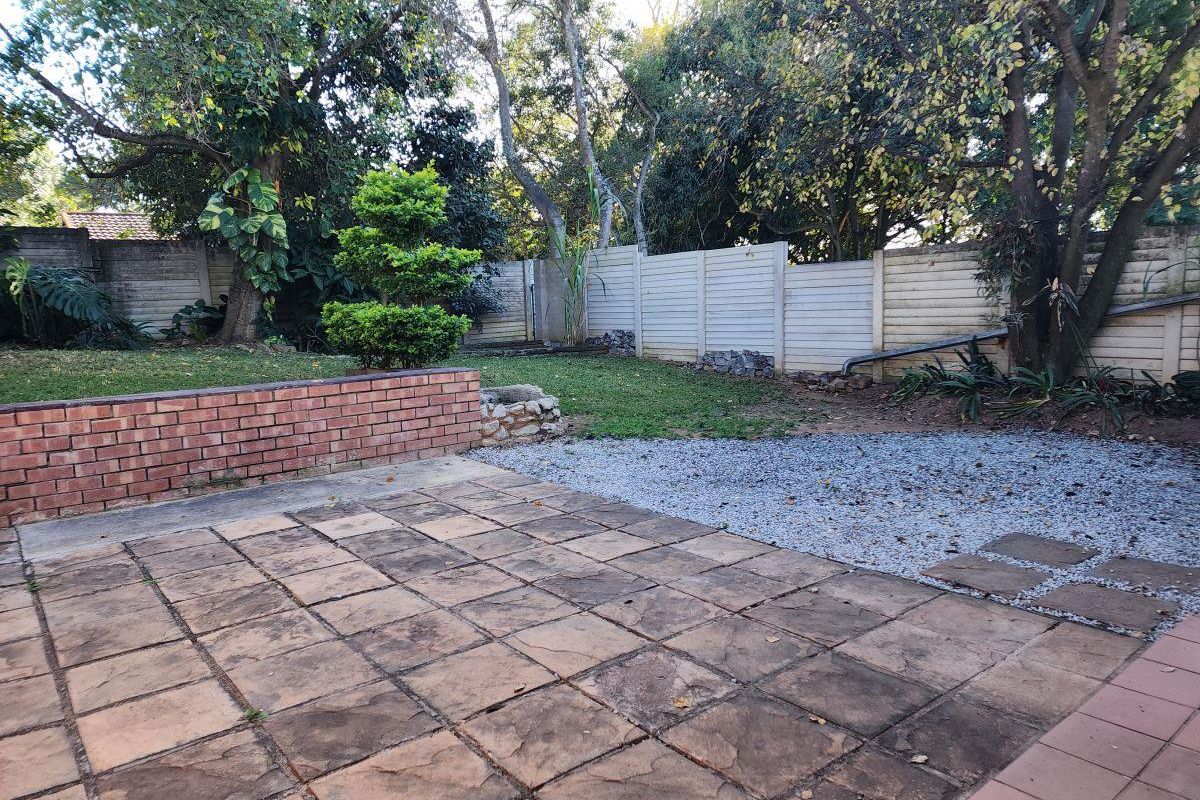 A private rear garden featuring a paved patio area, brick retaining wall, and established trees, offering potential for outdoor entertainment and landscaping.