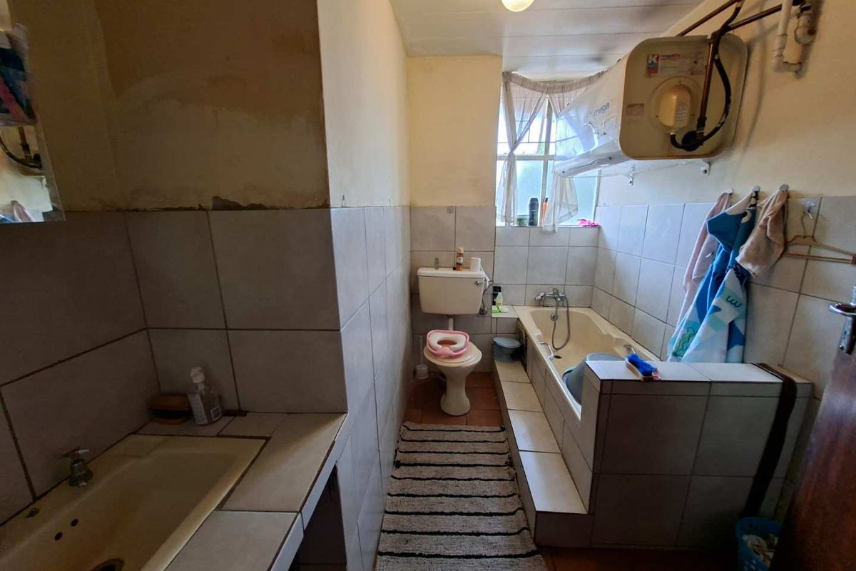 A dated bathroom featuring a built-in bathtub, toilet, and vanity basin with exposed water heater and tiled finishes.