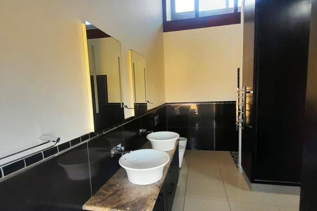 Modern bathroom featuring a double vanity with vessel sinks, stone countertop, dark cabinetry, and high-level windows providing natural light.