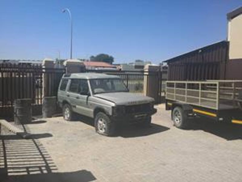 Industrial property exterior featuring a paved driveway, secure metal perimeter fencing, and metal cladding on the building structure.