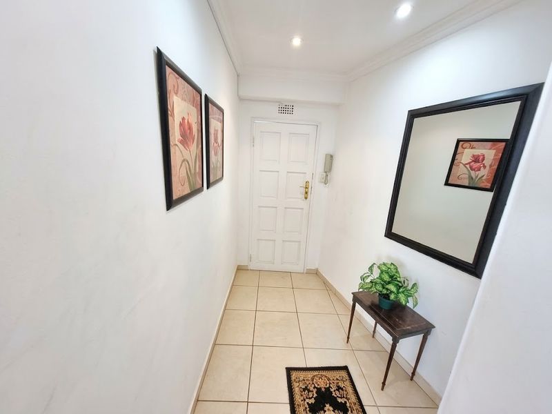 A clean and well-maintained entrance hallway featuring tiled flooring, recessed downlighting, and a secure intercom system.