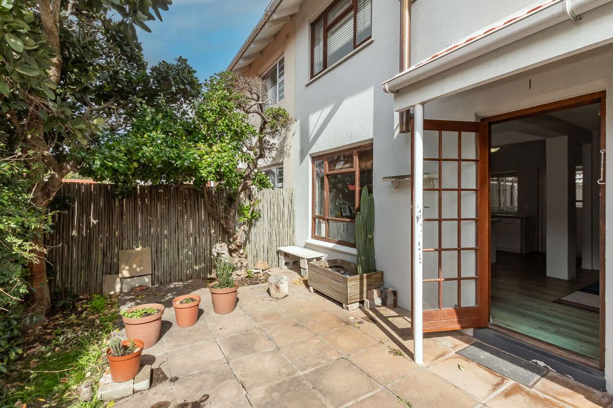 A rear patio area featuring paved flooring, a covered veranda section, and direct access to the interior through a timber-framed glass door.