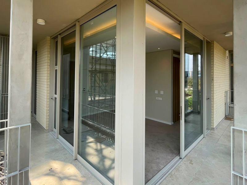 A modern covered balcony featuring large sliding glass doors, tiled flooring, and a metal balustrade, providing seamless indoor-outdoor flow.