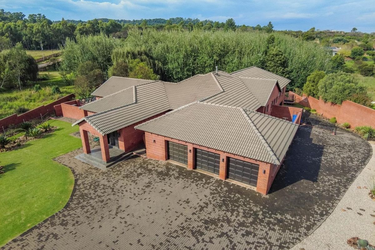 Aerial view of a spacious brick-faced residence featuring a triple garage, tiled roof, and expansive surrounding garden and driveway.