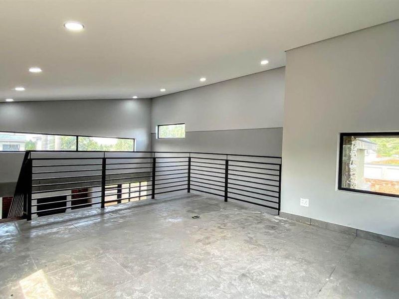 A spacious, modern open-plan living area featuring tiled floors, recessed lighting, a sleek metal balustrade, and contemporary architectural windows with exposed brick accents.
