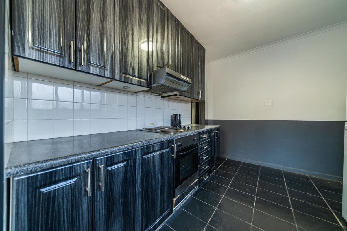 A functional kitchen featuring dark wood-grain cabinetry, granite countertops, built-in oven, electric hob, and tiled flooring with a neutral wall finish.