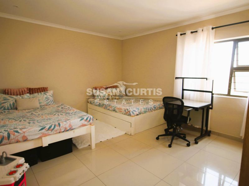 A spacious bedroom featuring neutral wall tones, tiled flooring, and a large window allowing for natural light.