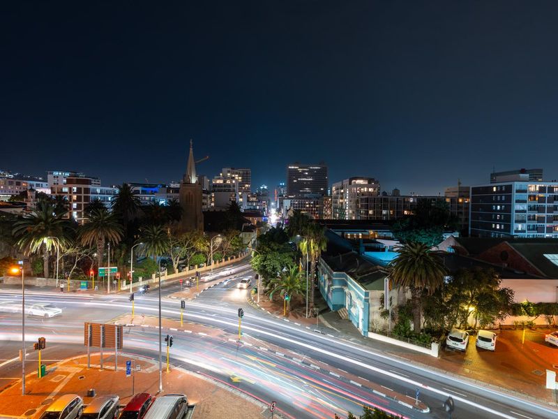 A night-time elevated view overlooking a busy urban intersection and surrounding city skyline.