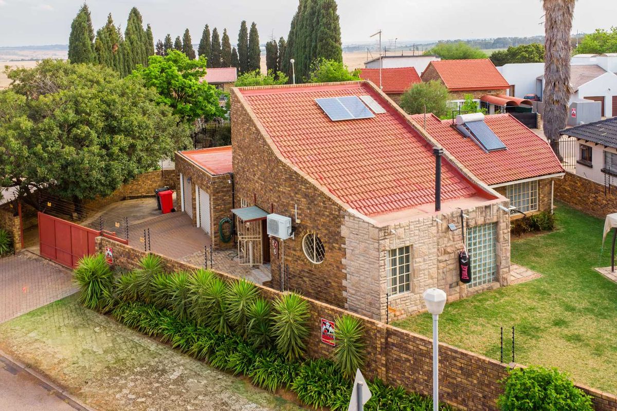 Aerial view of a residential property featuring a brick facade, tiled roof with solar installations, paved driveway, and a landscaped garden with perimeter security.