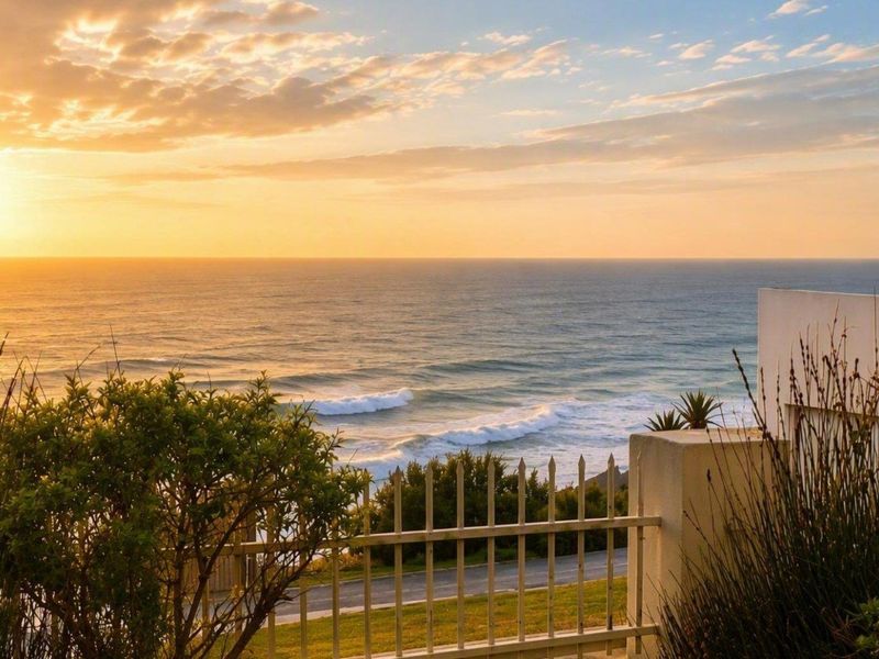 A scenic sunset view overlooking the ocean, featuring a coastal property boundary with metal fencing and masonry walling.
