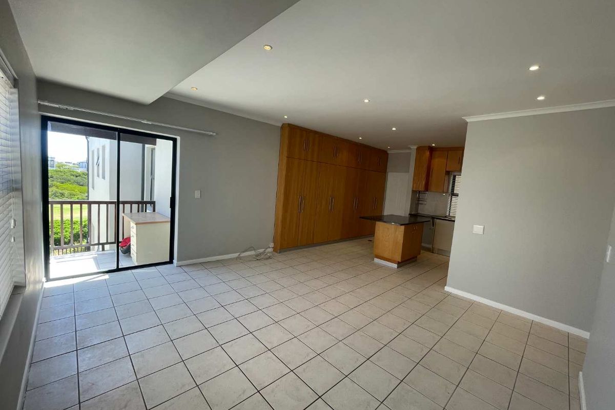 Spacious open-plan living and kitchen area featuring tiled floors, extensive built-in cabinetry, a central kitchen island, and access to a private balcony.