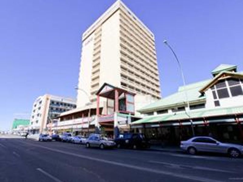 A street-level view of a multi-story commercial building featuring retail frontage and a covered pedestrian walkway along the main road.