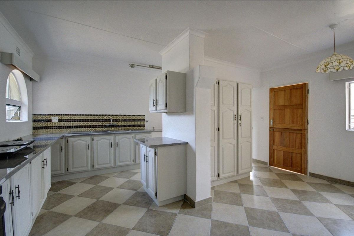 A functional kitchen featuring white cabinetry, a tiled splashback, and a central pillar, providing ample storage and a practical layout.