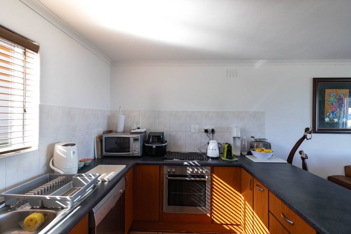 A functional kitchen featuring wooden cabinetry, dark laminate countertops, tiled splashbacks, and a built-in oven with a cooktop.