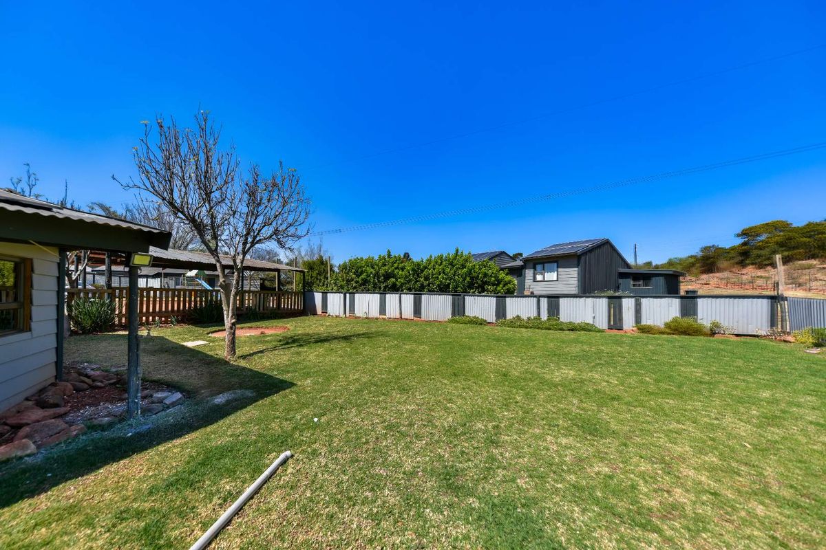 A spacious rear garden featuring a well-maintained lawn, corrugated metal perimeter fencing, and a covered patio area attached to the main dwelling.