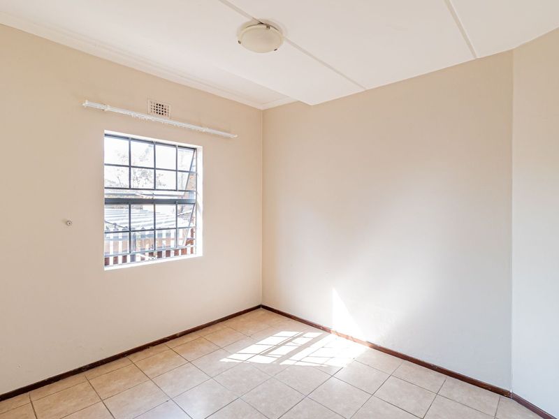 An empty bedroom featuring tiled flooring, a steel-framed window, and a ceiling-mounted light fixture, offering a blank canvas for renovation.