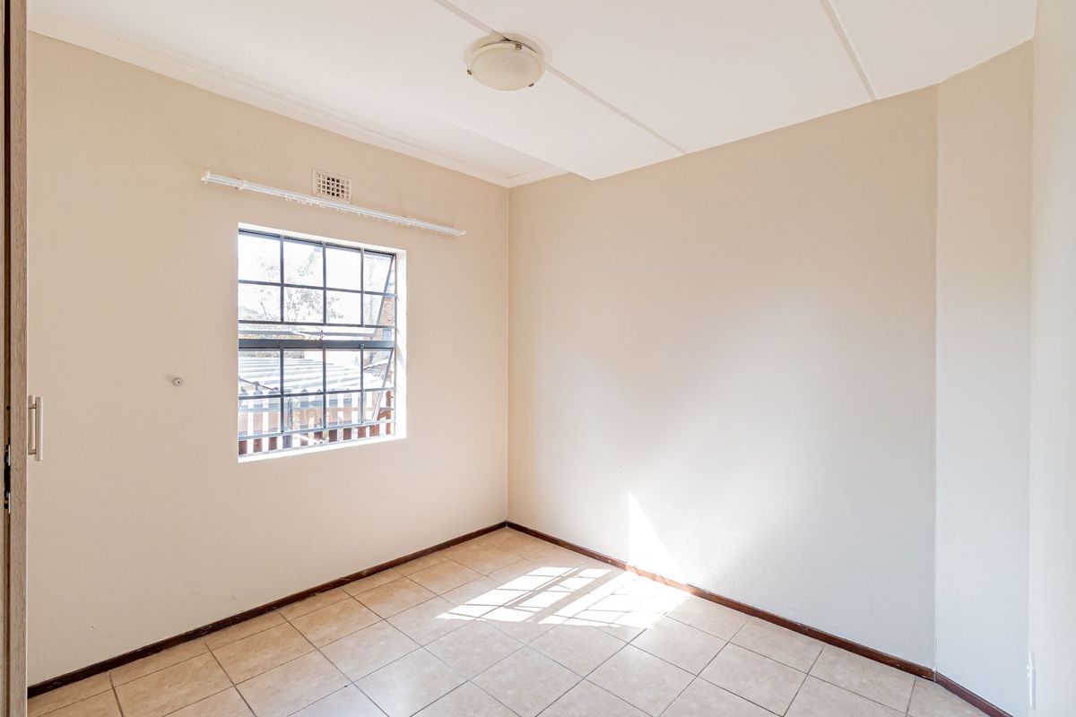 An empty bedroom featuring tiled flooring, a steel-framed window, and a ceiling-mounted light fixture, offering a blank canvas for renovation.
