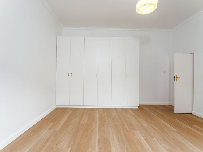 A bright, empty bedroom featuring light-toned laminate flooring, white walls, and ample built-in cupboard storage.