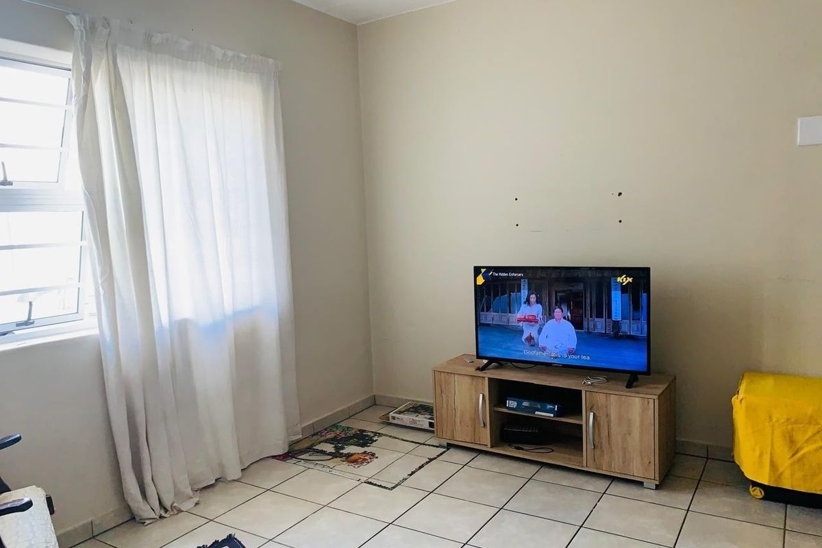 A living room area featuring neutral wall paint, tiled flooring, and a window with natural light.