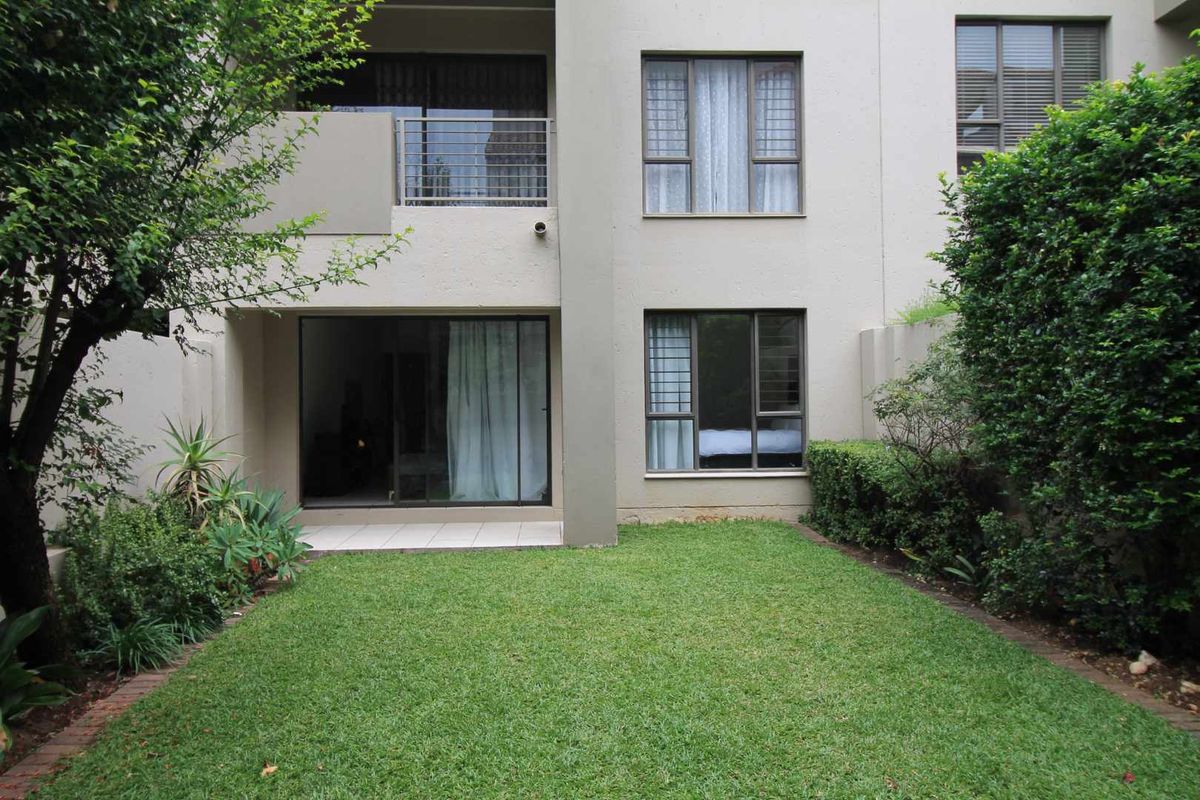 Rear view of the apartment featuring a private garden, tiled patio area, and sliding glass doors leading to the interior living space.