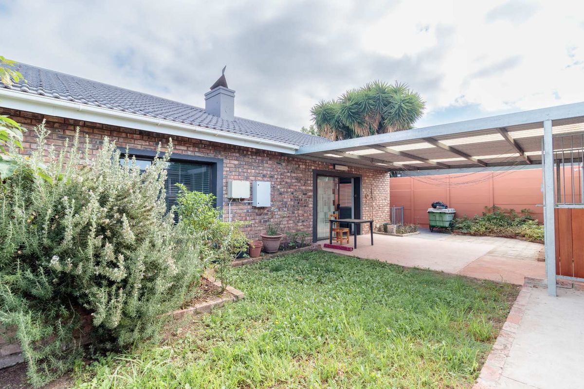 Rear view of the property featuring a brick facade, a covered patio area, and a metal carport structure adjacent to the garden.