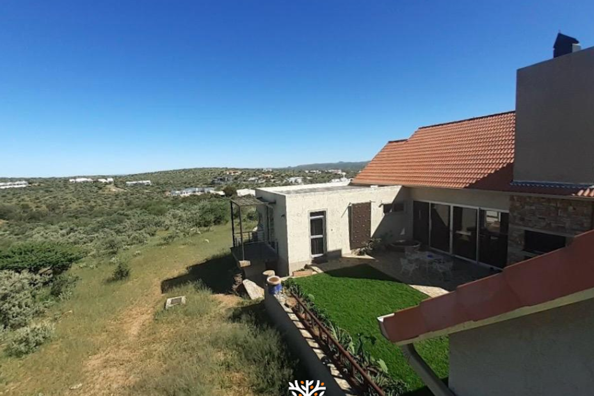 An elevated view of the rear exterior of the house, featuring a tiled roof, patio area, and a landscaped garden overlooking the surrounding landscape.