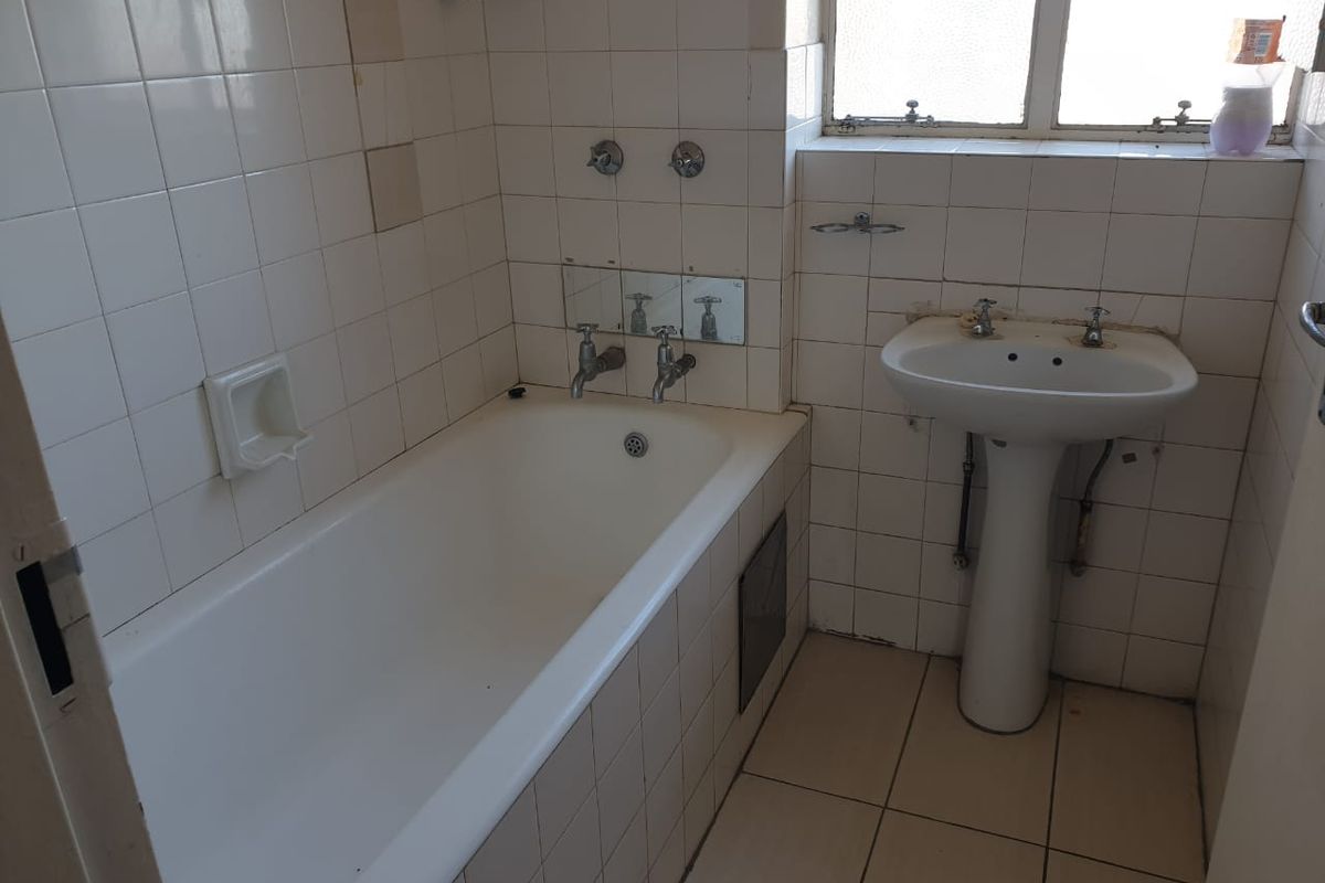 A dated bathroom featuring a standard bathtub, pedestal basin, and tiled walls. The space requires renovation to update the fixtures and finishes.