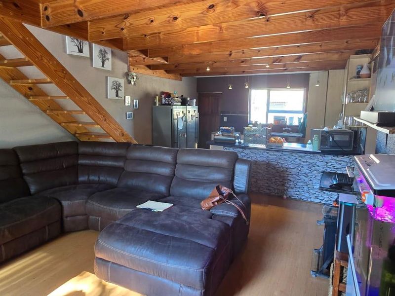 Open-plan living area featuring exposed timber ceiling beams, a wooden staircase, and a stone-clad breakfast bar connecting to the kitchen space.