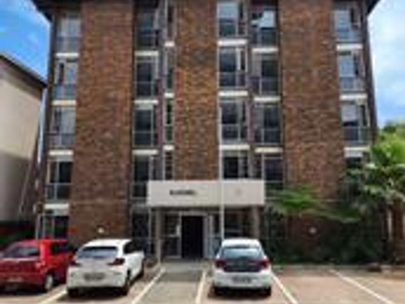 Front exterior view of a multi-story brick apartment building featuring a paved parking area and a covered entrance.