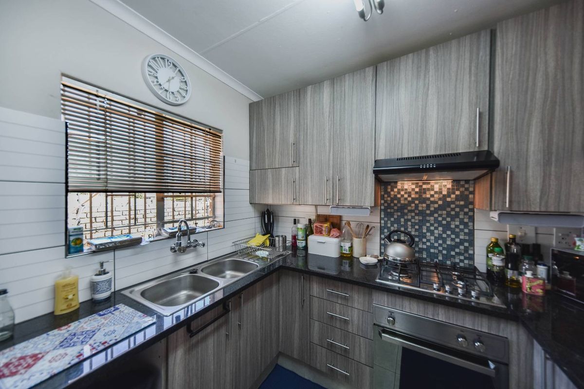 Modern kitchen featuring granite countertops, double basin sink, built-in oven, gas hob, extractor fan, and ample laminate cabinetry with mosaic tile backsplash.