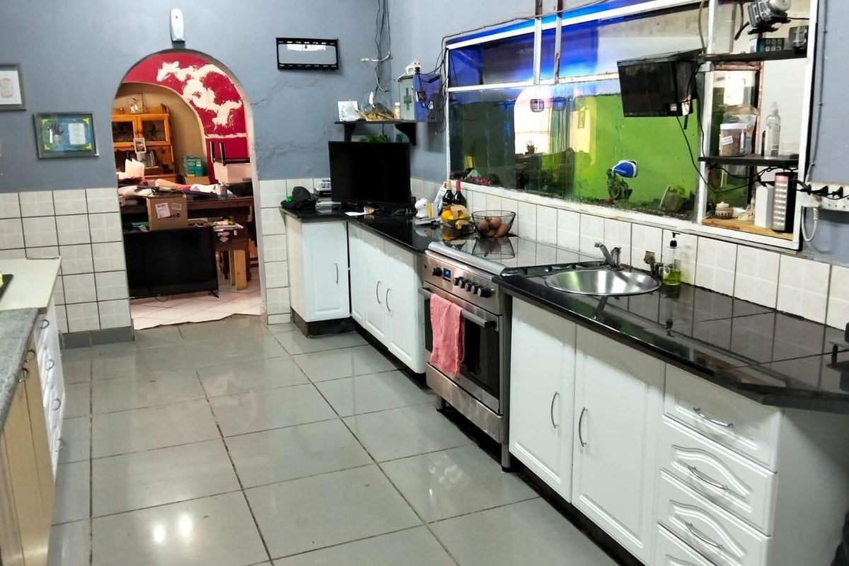 A functional kitchen featuring white cabinetry, black granite countertops, a stainless steel stove, and tiled flooring, with an arched entryway leading to adjacent living space.