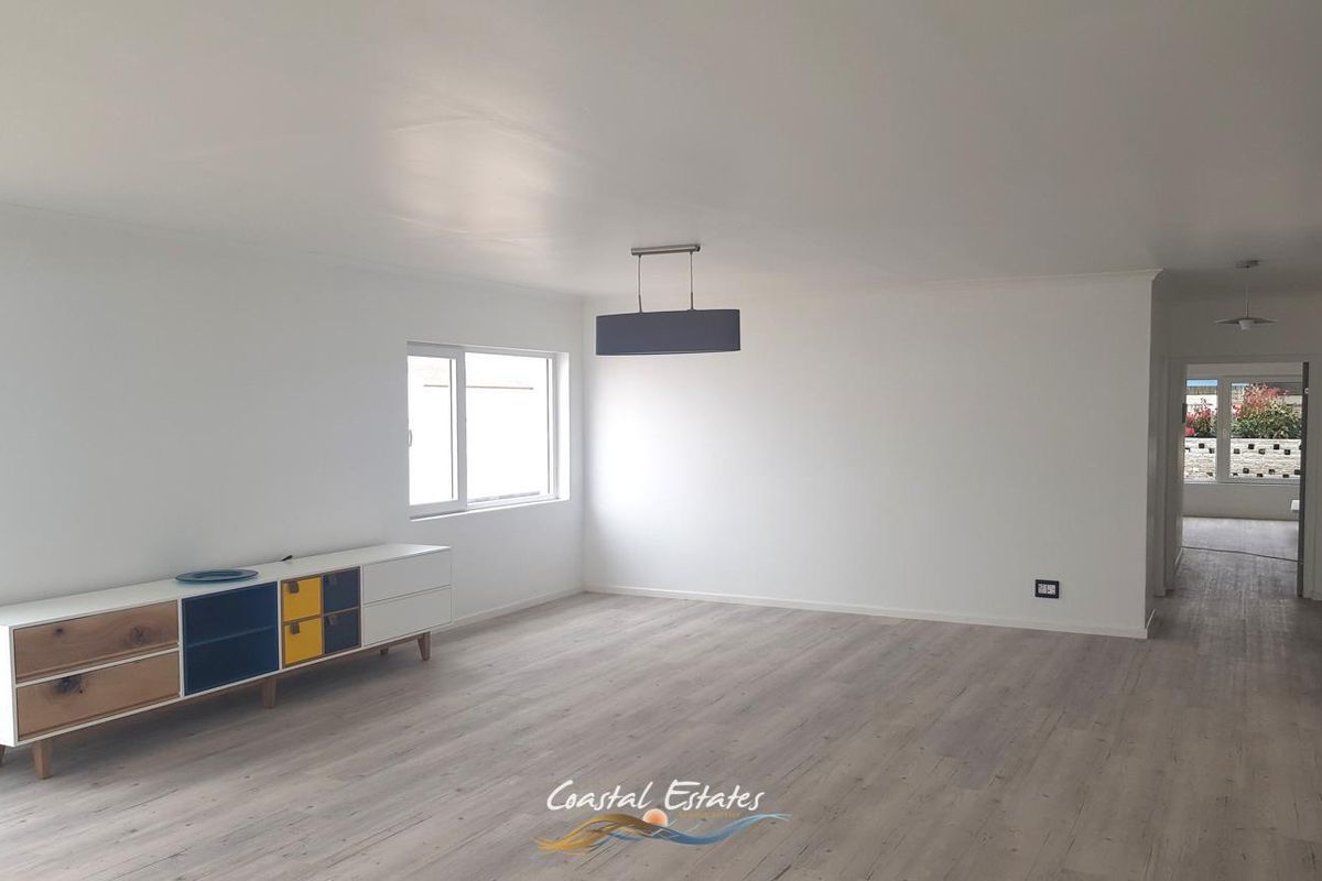 A bright, open-plan living area featuring modern laminate flooring, neutral walls, and a contemporary pendant light fixture.