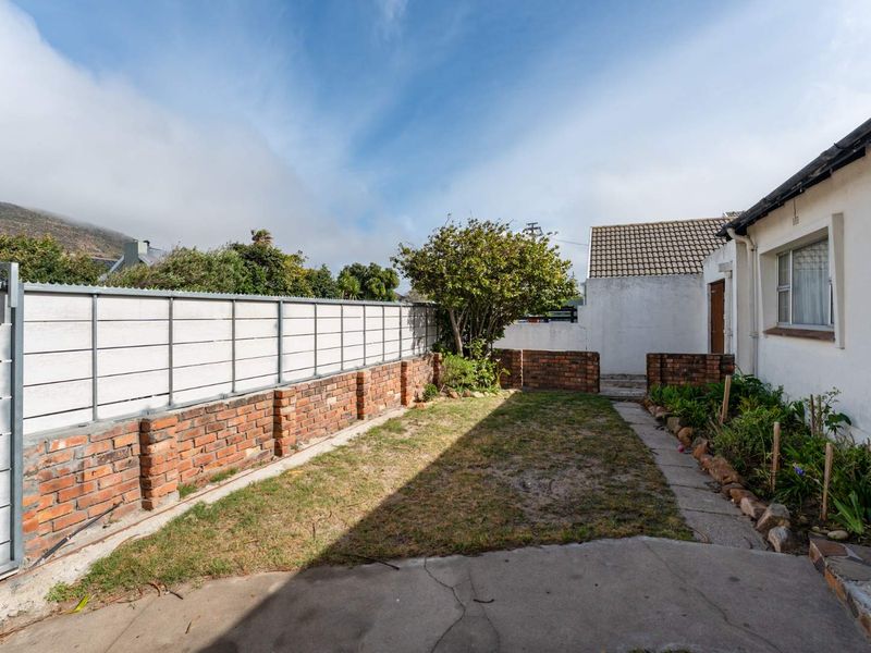 A rear garden area featuring a brick boundary wall, concrete paving, and a small lawn space adjacent to the main dwelling.