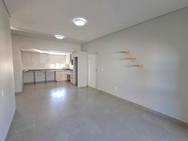 Modern open-plan living area featuring a sleek kitchen with subway tile backsplash, built-in cabinetry, and tiled flooring throughout.