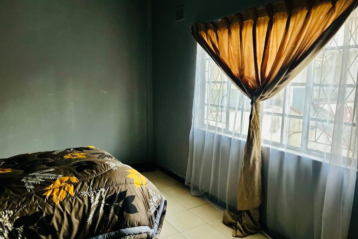 A bedroom featuring tiled flooring and a large window with security bars, providing natural light to the space.