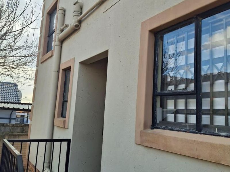 Rear exterior view of the property featuring a tiled balcony, metal security bars on windows, and visible external plumbing infrastructure.