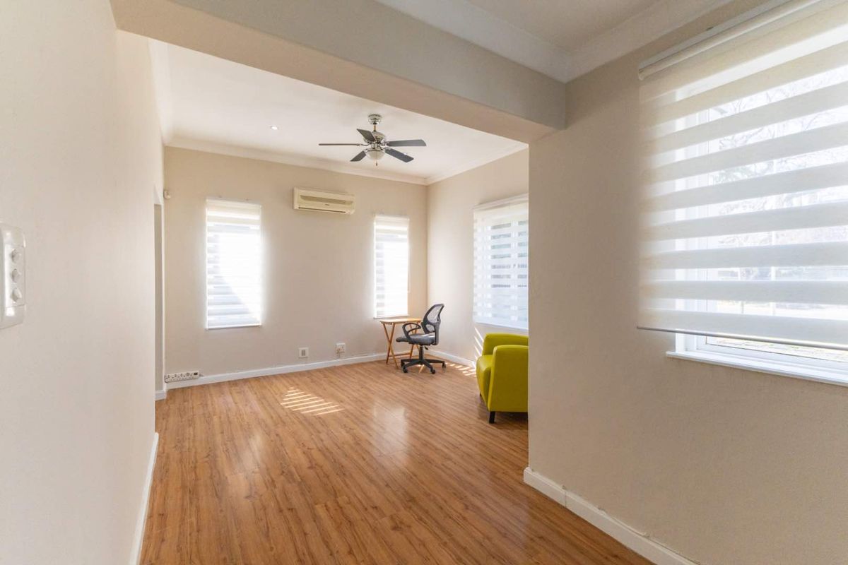 A bright living area featuring laminate flooring, a ceiling fan, and a wall-mounted air conditioning unit with modern roller blinds.