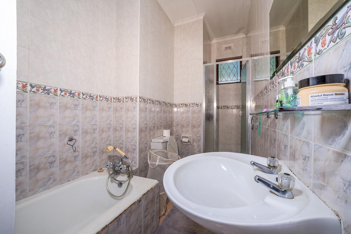 A functional bathroom featuring a bathtub, separate shower enclosure, pedestal basin, and toilet, finished with dated ceramic wall tiles.