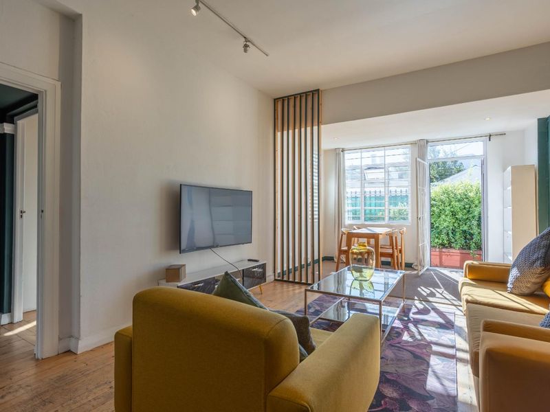 Bright living room featuring timber flooring, a decorative timber slat room divider, and direct access to an outdoor patio area through a glass door.